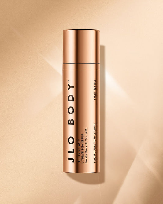 Gold bottle of JLO Body body serum on a beige background