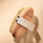 Wooden brush with bristles and a strap labeled 'JLO BEAUTY' on a beige background